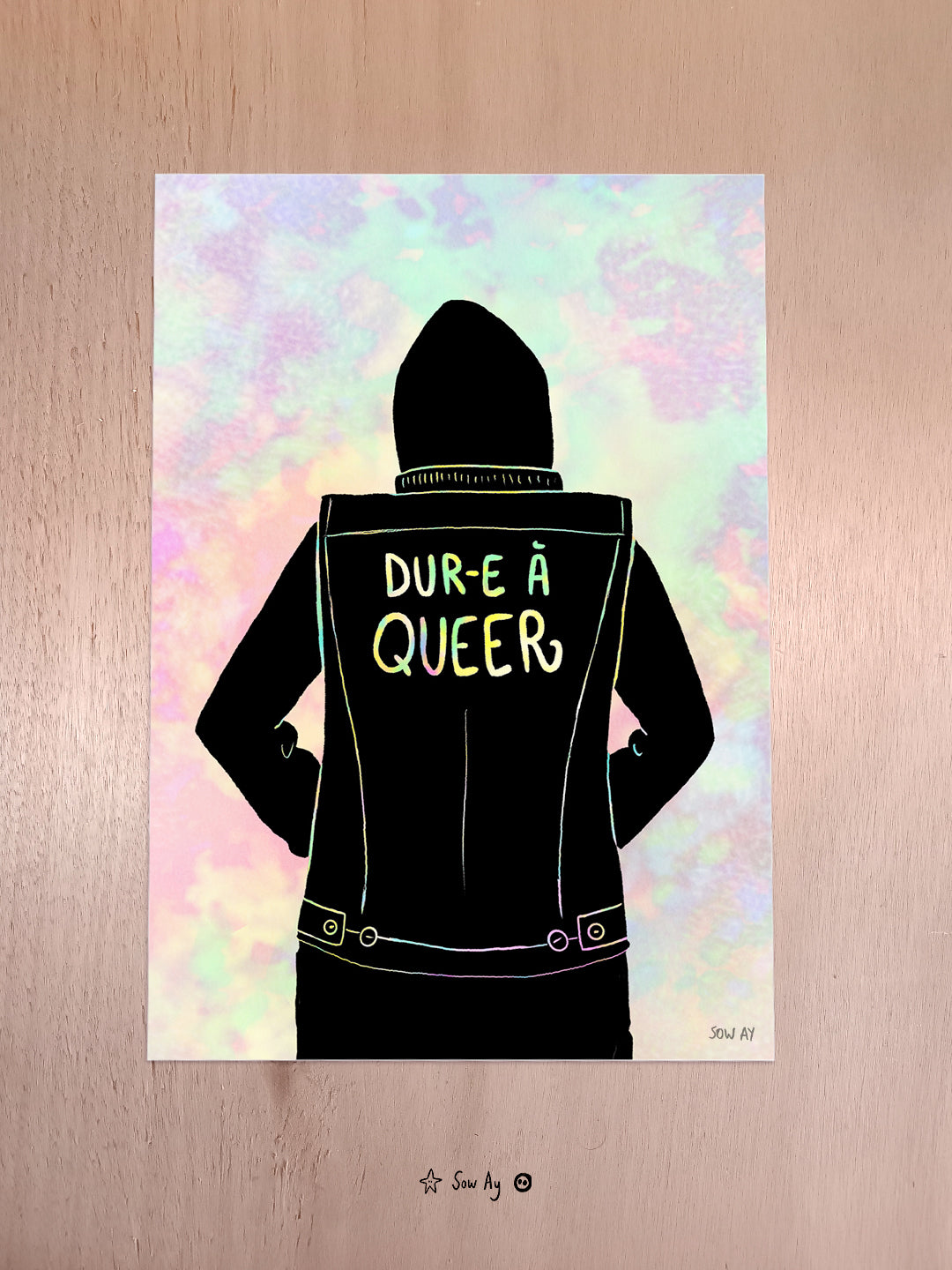 un personnage de dos qui porte une veste noire sur laquelle est écrit "dur-e à queer". Le fond est de couleur pastel, comme le texte.