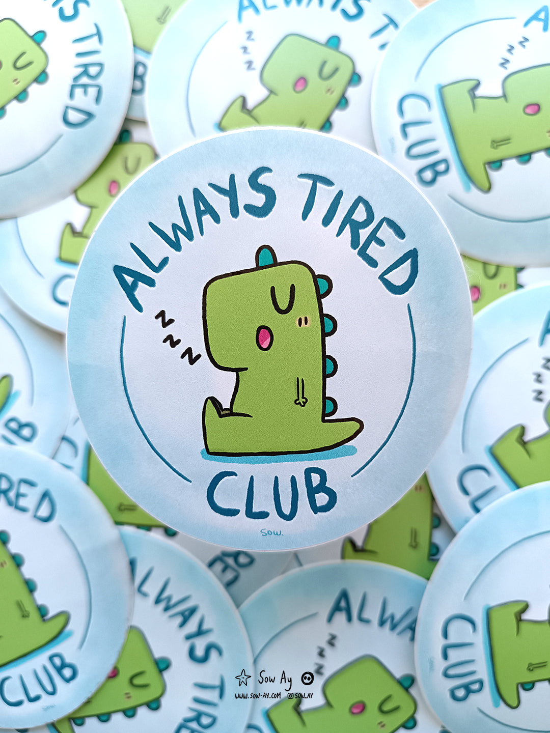 dinosaure vert assis, de profil, qui s'est endormi la bouche ouverte. Autour de lui est inscrit : "always tired club"