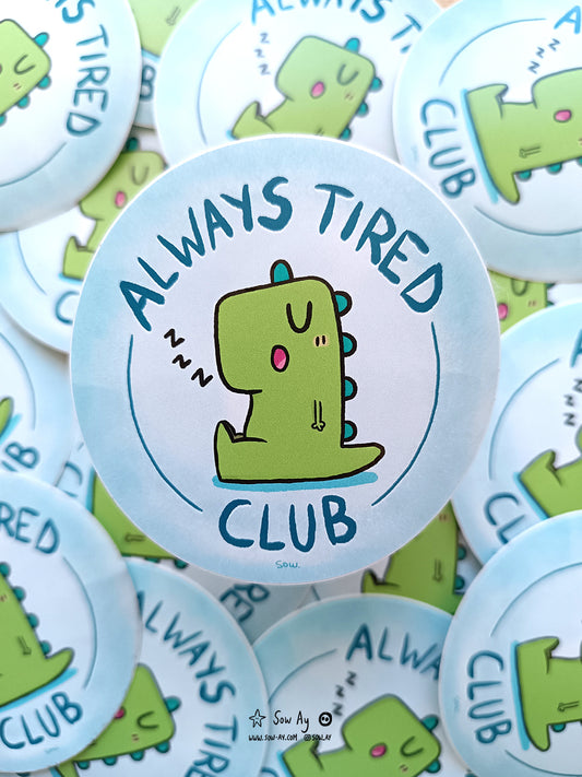 dinosaure vert assis, de profil, qui s'est endormi la bouche ouverte. Autour de lui est inscrit : "always tired club"