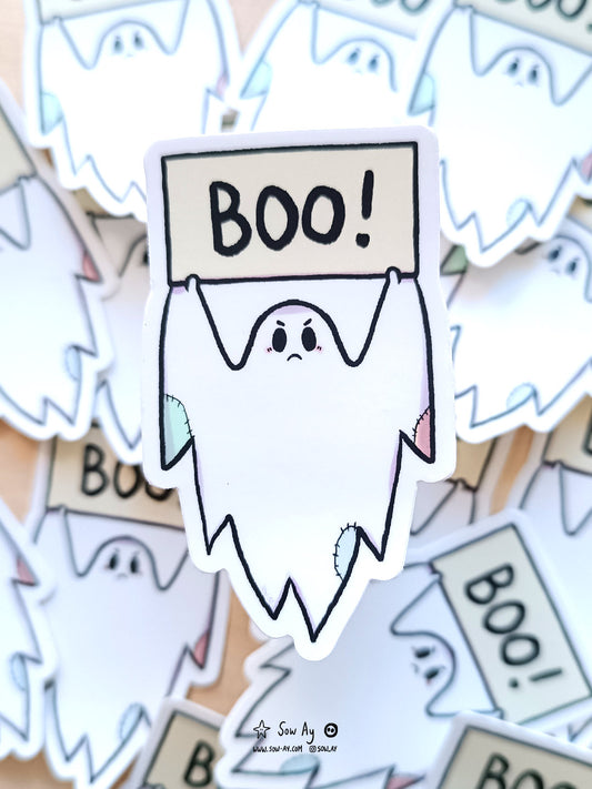 fantôme au look rapiécé qui tient en l'air une pancarte sur laquelle est inscrit le mot "BOO !". Le fantôme est en colère.