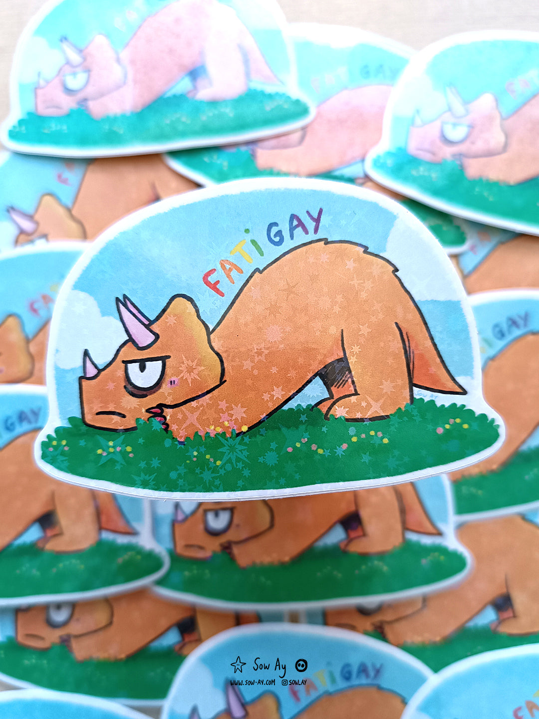 tricératops orange de profil, avec une expression fâché sur le visage. Au dessus est écrit fatigay aux couleurs du drapeau LGBTQIA+