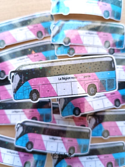 bus de profil de la région auvergne rhônes alpes aux couleurs du drapeau transgenre bleu rose et blanc, sur lequel est écrit en noir "la région vous transporte" et "trans" est écrit en blanc et se détache