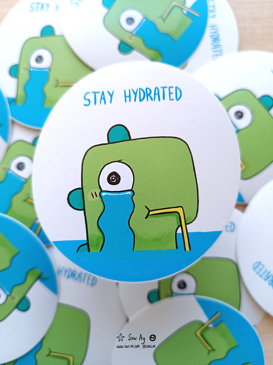 on voit un dinosaure vert immergé dans l'eau, seule sa tête dépasse. Il pleure et l'eau dans laquelle il baigne son ses larmes. Il a une paille dans la bouche pour boire ses larmes. Il est écrit "stay hydrated"